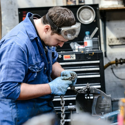 Person in blue work overalls inspecting chains in the workshop